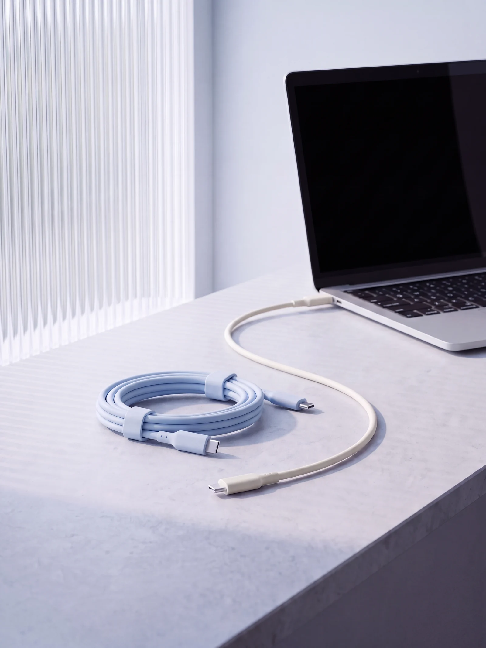Cream white and baby blue SCIGOLD silicone USB-C cables on a stone ledge beside an open laptop