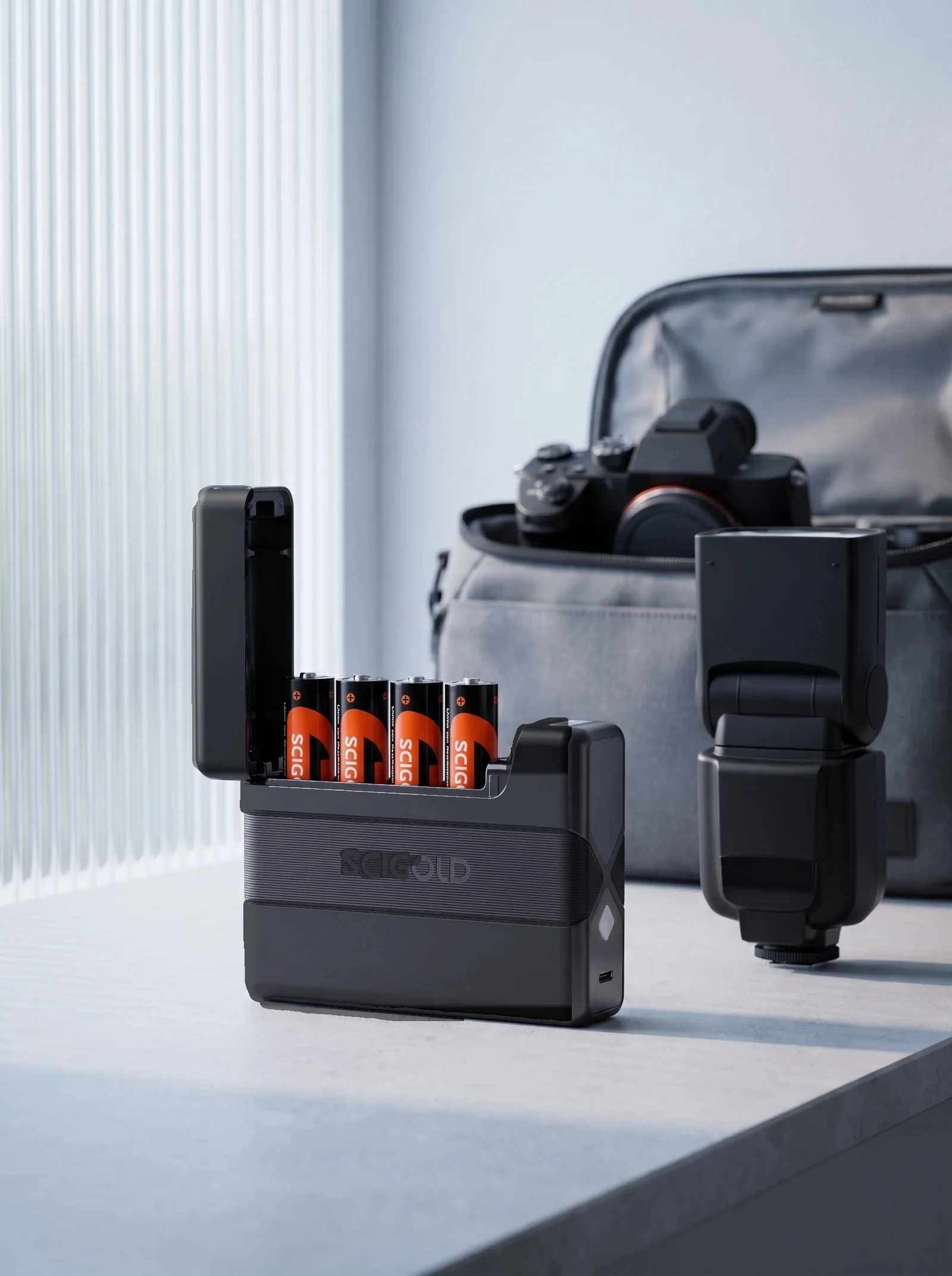SCIGOLD Pocket Charging Case with four AA cells on a desk beside a camera flash and a camera bag