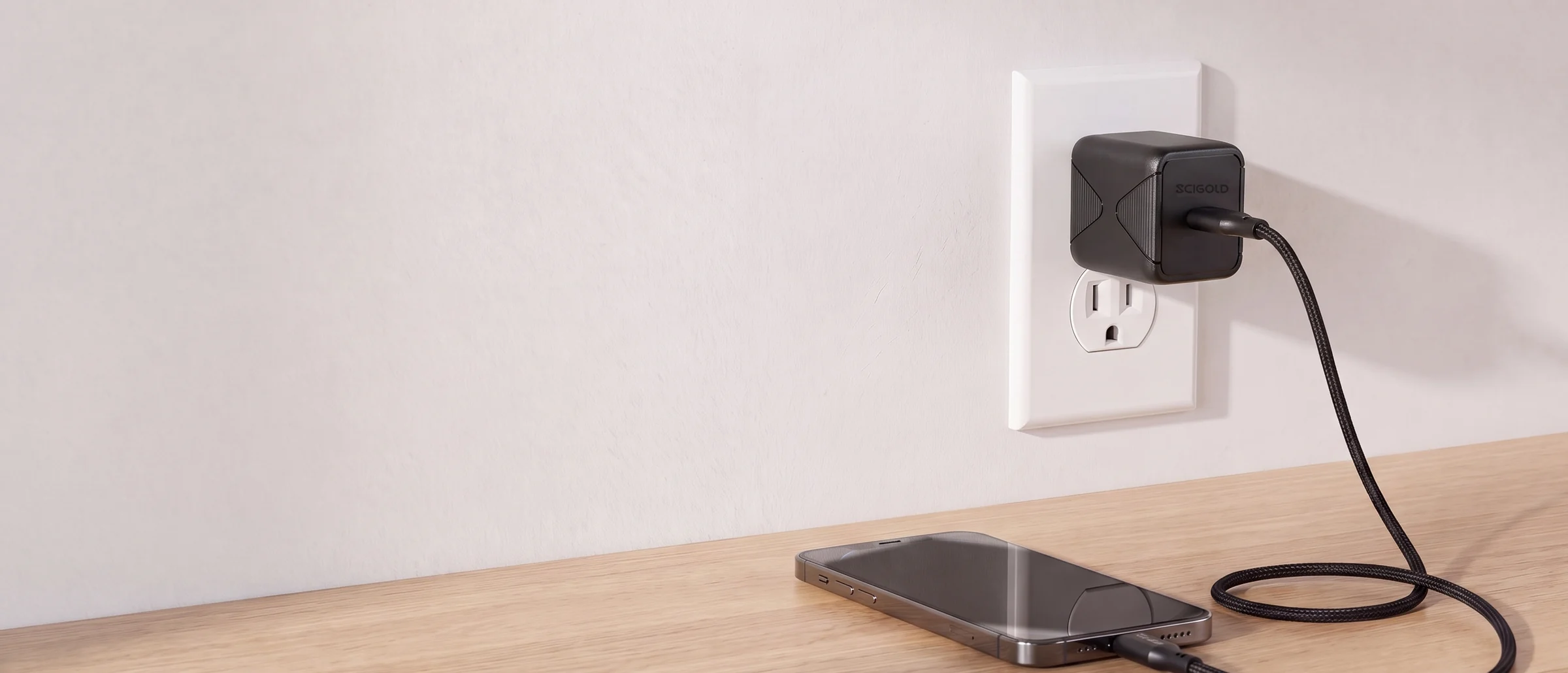 SCIGOLD 45W charger in a wall outlet by a desk, charging a phone